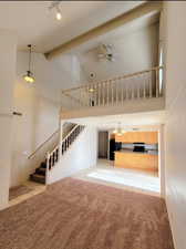 Living room featuring beamed ceiling, light colored carpet, ceiling fan with notable chandelier, and high vaulted ceiling