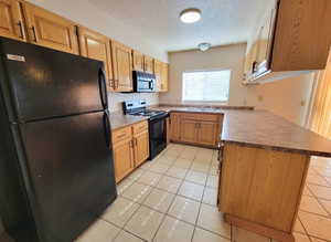 Kitchen featuring black appliances, a textured ceiling, sink, and light tile floors