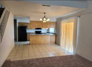 Kitchen with black appliances, a notable chandelier, hanging light fixtures, and light carpet