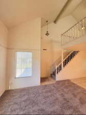 Carpeted empty room with beamed ceiling and high vaulted ceiling