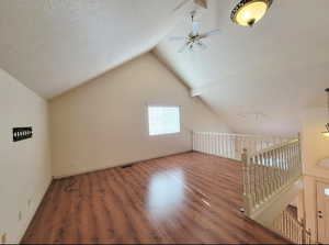 Bonus room featuring ceiling fan, dark hardwood / wood-style floors, vaulted ceiling, and a textured ceiling