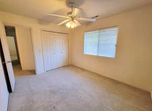 Unfurnished bedroom with ceiling fan, a closet, and light colored carpet