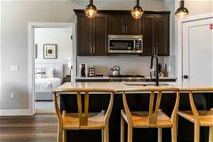 Kitchen with sink, pendant lighting, tasteful backsplash, dark hardwood / wood-style flooring, and a kitchen breakfast bar