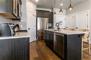Kitchen with an island with sink, sink, appliances with stainless steel finishes, decorative light fixtures, and dark hardwood / wood-style floors