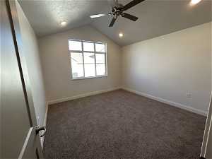 Carpeted empty room with ceiling fan, a textured ceiling, and vaulted ceiling