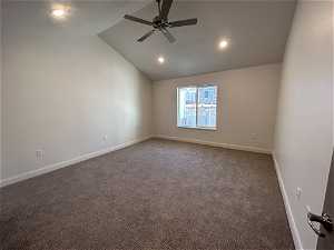 Empty room with dark carpet, lofted ceiling, and ceiling fan