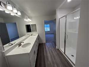 Bathroom with dual bowl vanity, a shower with shower door, and hardwood / wood-style flooring