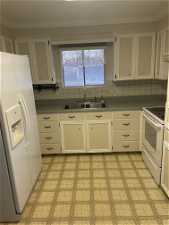 Kitchen with sink, white appliances, white cabinets, ornamental molding, and tasteful backsplash