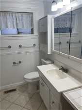 Bathroom featuring toilet, tile floors, vanity with extensive cabinet space, and crown molding