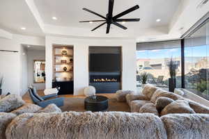 Living room with a raised ceiling, built in shelves, ceiling fan, and hardwood / wood-style flooring