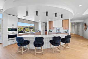 Kitchen with a center island, double oven, light wood-type flooring, and white cabinetry