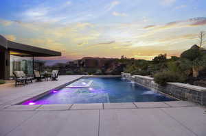 Pool at dusk featuring pool water feature and a patio