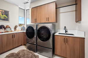 Washroom featuring washing machine and clothes dryer, cabinets, sink, and light tile floors