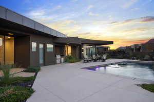 Pool at dusk featuring a patio, exterior kitchen, and a grill