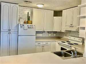 Kitchen featuring white appliances, premium range hood, white cabinetry, and backsplash