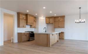 Kitchen with gas range, an island with sink, tasteful backsplash, and light hardwood / wood-style floors