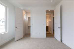 Unfurnished bedroom featuring multiple windows, a walk in closet, light carpet, and a closet