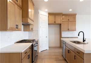 Kitchen with an island with sink, sink, appliances with stainless steel finishes, tasteful backsplash, and light hardwood / wood-style flooring