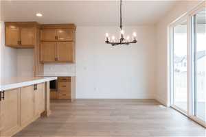 Kitchen with a healthy amount of sunlight, an inviting chandelier, light hardwood / wood-style flooring, and backsplash