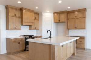 Kitchen with tasteful backsplash, sink, light wood-type flooring, and stainless steel range with gas cooktop