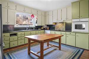 Kitchen featuring green cabinets, hardwood / wood-style floors, oven, and backsplash