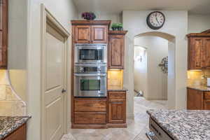 Kitchen with light tile floors, dark stone countertops, stainless steel appliances, and backsplash