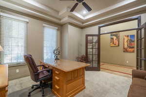 Office space with a raised ceiling, light carpet, and ceiling fan