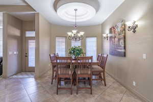 Dining area with a raised ceiling, an inviting chandelier, and light tile flooring