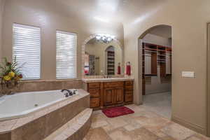 Bathroom with a notable chandelier, tile floors, tiled tub, and vanity