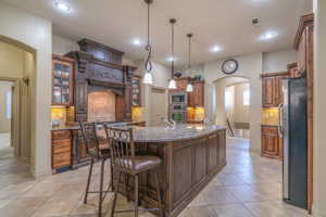 Kitchen with hanging light fixtures, a kitchen island with sink, tasteful backsplash, stainless steel appliances, and light tile floors