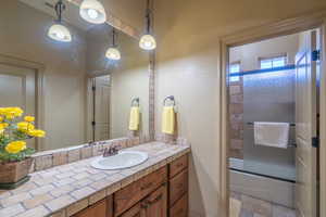 Bathroom with vanity with extensive cabinet space, tile flooring, and shower / bath combination with glass door