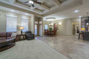 Living room featuring beamed ceiling, coffered ceiling, ceiling fan with notable chandelier, and light carpet