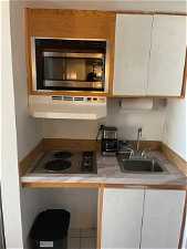 Kitchen with stainless steel microwave, sink, ventilation hood, electric stovetop, and white cabinetry