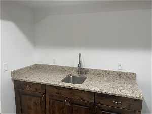 Basement Kitchenette with dark brown cabinets, sink, and light stone countertops