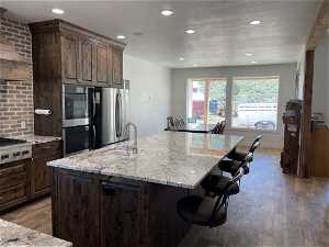 Kitchen featuring stainless steel refrigerator, light stone counters, hardwood / wood-style flooring, a kitchen island with sink, and a kitchen bar