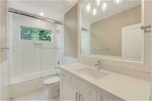 Full bathroom with vanity with extensive cabinet space, enclosed tub / shower combo, toilet, and tile flooring