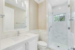 Bathroom featuring tile walls, a shower with door, toilet, and vanity