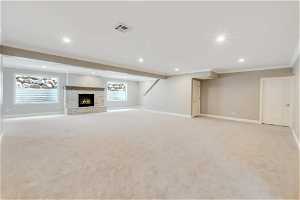 Basement featuring ornamental molding, light colored carpet, and a stone fireplace