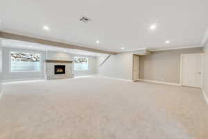 Basement featuring ornamental molding, light colored carpet, and a stone fireplace