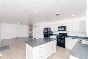 Kitchen featuring black appliances, light LVP flooring, a center island, and white cabinets