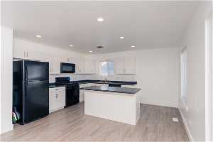 Kitchen featuring a center island, sink, light LVP flooring, black appliances, and white cabinetry