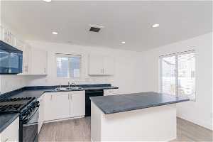 Kitchen featuring black appliances, light LVP flooring, a kitchen island, and white cabinets