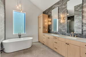 Bathroom with double sink vanity, vaulted ceiling, a tub, tile walls, and tile flooring