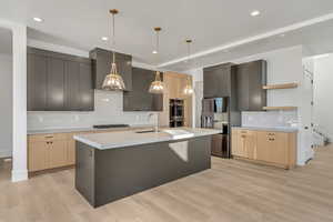 Kitchen featuring light wood-type flooring, a kitchen island with sink, hanging light fixtures, and tasteful backsplash