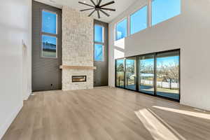 Unfurnished living room featuring light wood-type flooring, ceiling fan, a stone fireplace, and a high ceiling