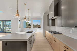 Kitchen with sink, a kitchen island with sink, tasteful backsplash, decorative light fixtures, and light hardwood / wood-style flooring