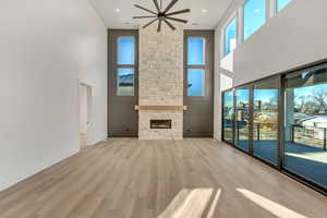 Unfurnished living room featuring ceiling fan, light hardwood / wood-style floors, a stone fireplace, and a towering ceiling