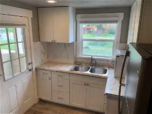 Kitchen featuring sink, hardwood / wood-style flooring, stainless steel fridge, white cabinets, and tasteful backsplash