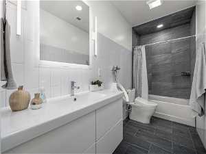 Full bathroom with shower / bathtub combination with curtain, tile walls, large vanity, tile flooring, and toilet