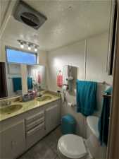 Bathroom with toilet, a textured ceiling, dual sinks, vanity with extensive cabinet space, and tile flooring
